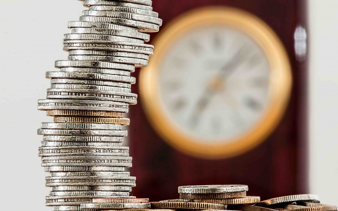 A stack of coins in focus, with an out-of-focus clock in the background. To illustrate types of IRA