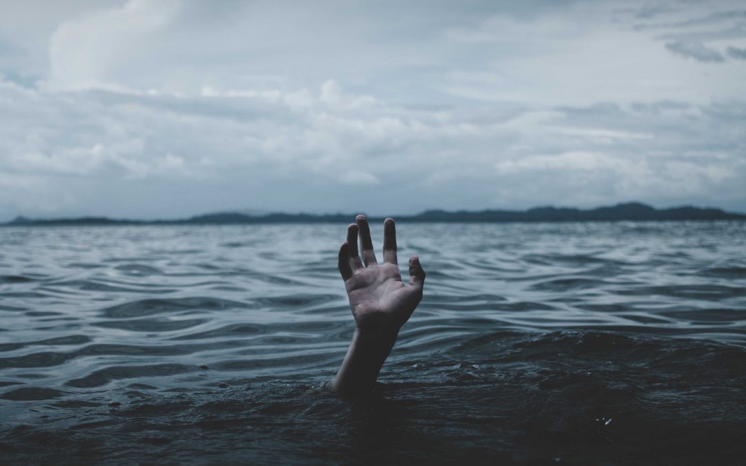 A hand rises from the sea to illustrate a person sinking in too much debt.